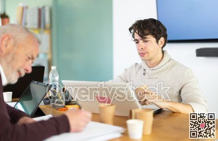 Young man working on laptop, elderly man takes notes on documents