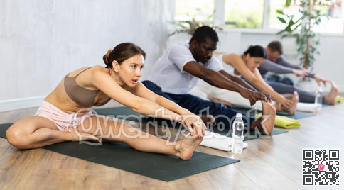 Young woman performing Janu Sirsasana with group in yoga studio