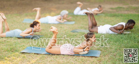 Multinational yoga enthusiasts with female coach perform dhanurasana in park