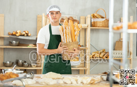 Happy male baker posing with basket of freshly baked baguettes in bakery, demonstrating concept of food industry and baker profession
