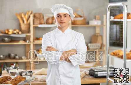 Portrait of positive male baker in uniform in bakery kitchen