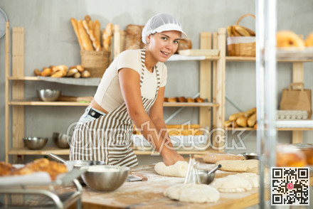 Young female baker kneading dough on flour-dusted table in artisan bakery