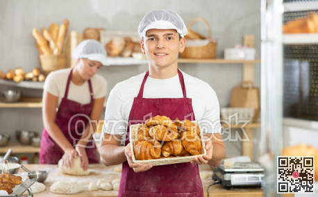 Young male baker holding croissants in square wicker basket