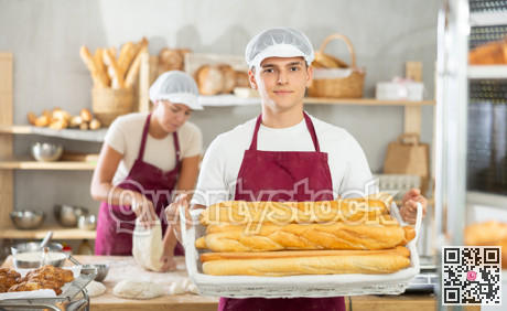 Dedicated young baker offering freshly baked baguettes in bakery