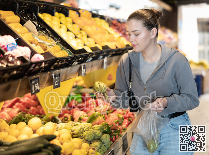 Young woman choosing artichoke in vegetable shop