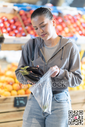Young woman choosing eggplants at vegetable shop
