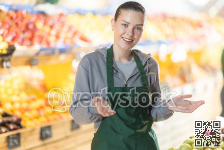 Young female shop assistant inviting in vegetable store