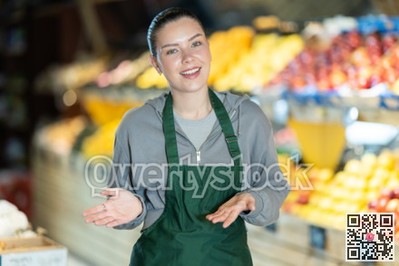 Young female shop assistant inviting in vegetable store