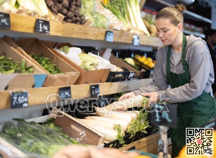 Young woman seller puts daikon in vegetable shop