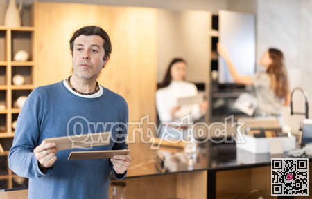 Male buyer with samples of material chooses kitchen set in furniture store