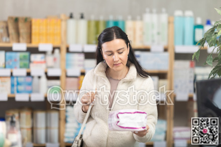 Middle-aged woman customer choosing feminine pads in drugstore