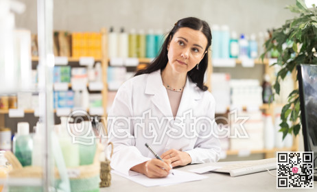Female pharmacist working at computer and filling out papers