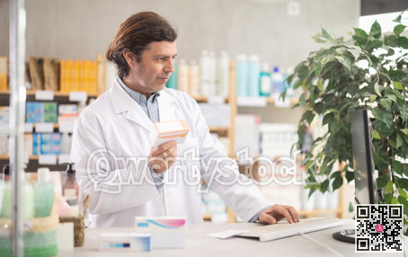 Friendly male pharmacist standing at drugstore with medical product in hands