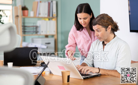 Middle-aged woman helping male colleague with tasks on laptop