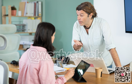 Man working on laptop scolding woman with tablet in office