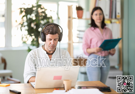 Middle-aged man wearing earphones working with laptop in office