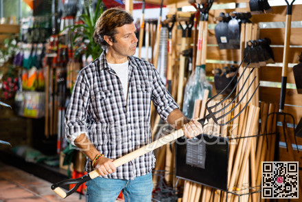 Adult gardener choosing pitchfork in garden tools store
