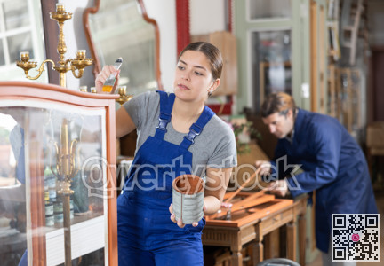 Professional furniture restorer renewing vintage chest of drawers in workshop