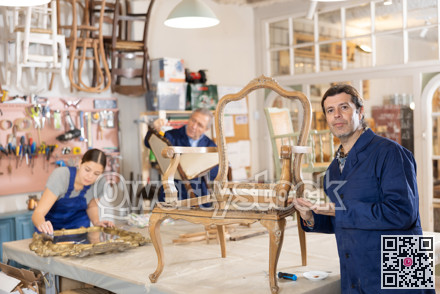 Skilled middle-aged male furniture repair specialist in uniform restoring Victorian chair during workday in workshop