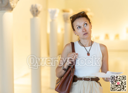 Focused woman visitor with booklet in her hands examines exhibit standing in art gallery