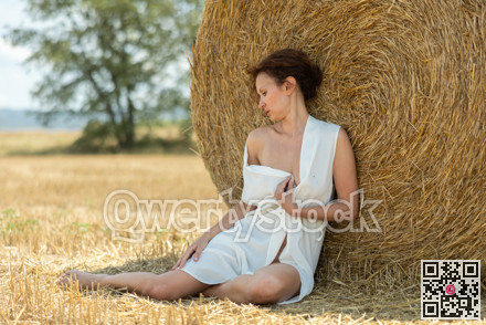Woman with loose hair relaxing near hay bales on summer farm field