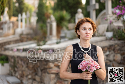 Woman in mourning black dress standing in cemetery with flowers