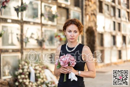 Woman in black mourning dress standing with flowers near columbarium