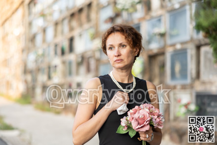 Drieving woman in black dress standing with bouquet by columbarium