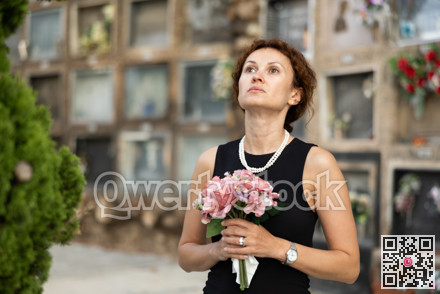 Woman in black mourning dress standing with flowers near columbarium