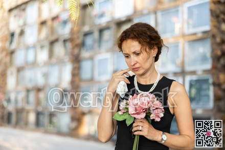 Upset woman in black dress, who lost loved one, brings flowers to grave
