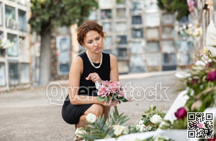 Grieving woman in black placing bouquet on grave