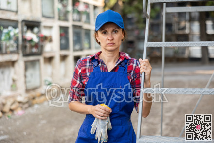 Female cemetery worker standing near columbarium wall