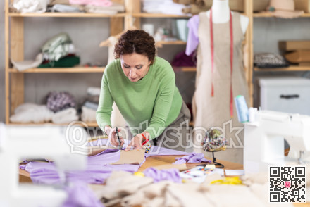 Female dressmaker cutting fabric with scissors while working in sewing workshop