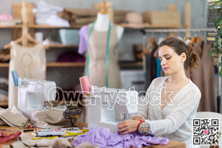Working in sewing workshop - female dressmaker working at sewing machine making stitches on fabric