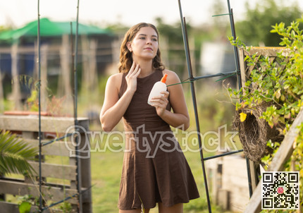 Young girl spraying mosquito repellent on herself on summer day at farm