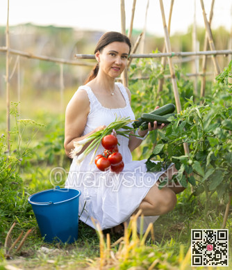 Woman in white dress with ripe vegetables in her hands - tomatoes, zucchini and green onions