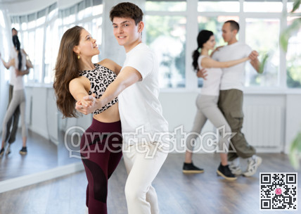 Young girls dancing together with guy slow ballroom dances in pairs in ball room at dance salon