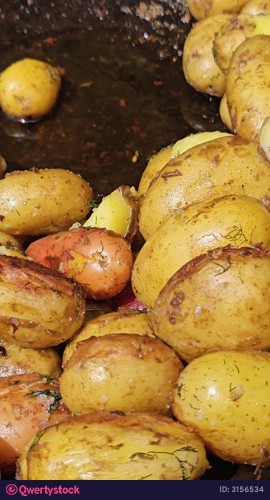 Close-up of golden roasted potatoes in a pan, emphasizing their crispy texture and rich color, as the camera zooms in to capture the cooking