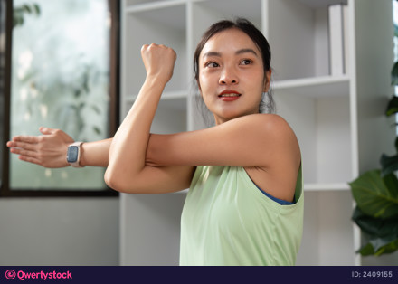 Fitness and Stretching. A woman engages in a stretching exercise at home, focusing on her arm and shoulder strength. photo 2409155