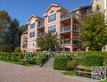 Apartement building on sunny day with bench and paved walkway in front