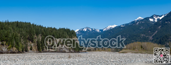 Panoramic view of Rocky mountains in British Columbia with drying-up river bed in front